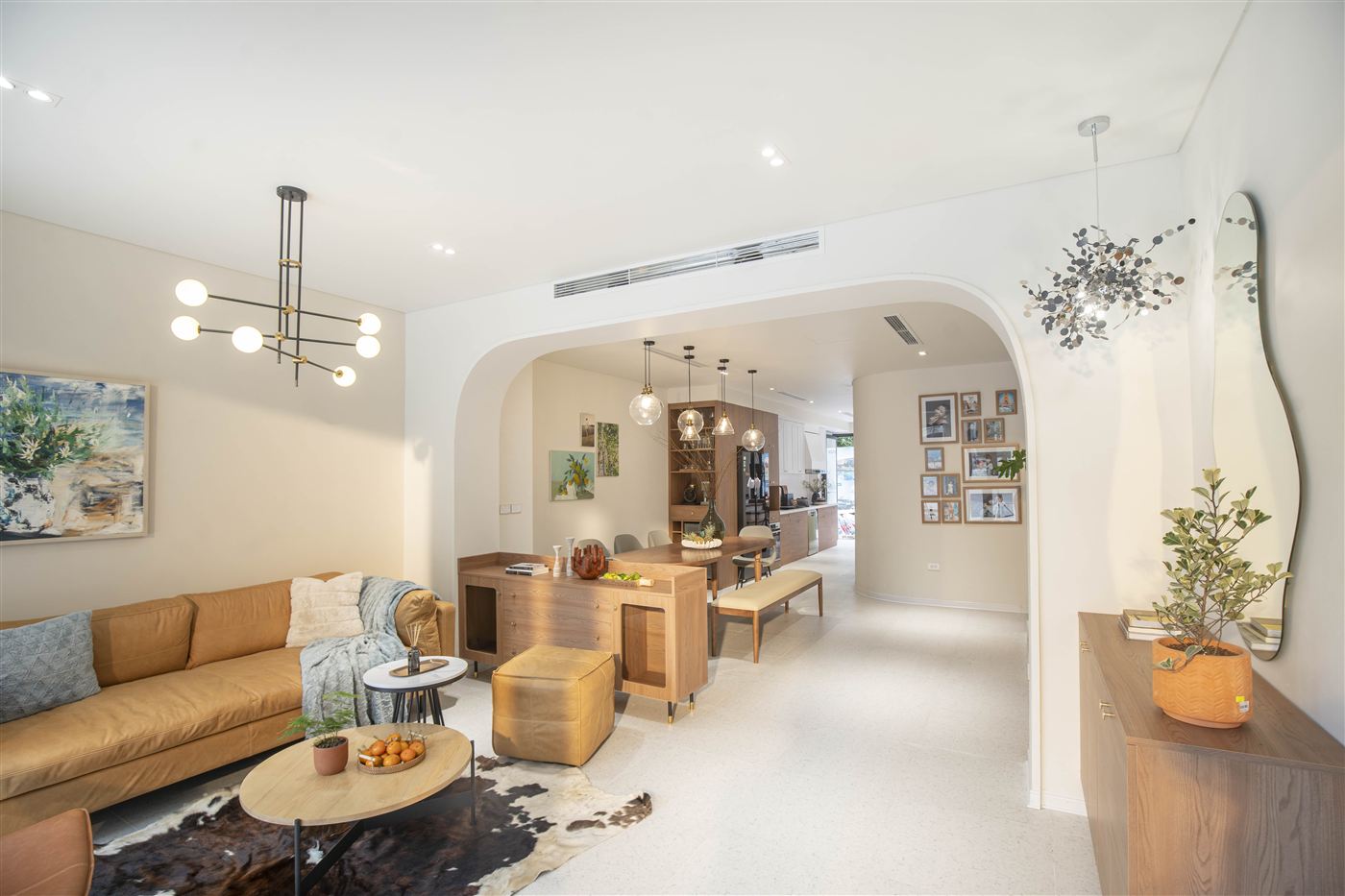 Phòng khách sofa da nâu, đèn chùm nhánh, gương lượn sóng